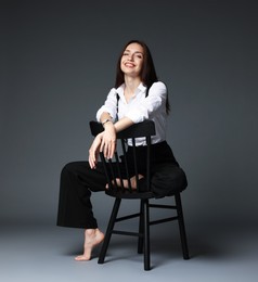 Photo of Beautiful woman in stylish outfit sitting on chair against grey background