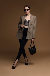 Photo of Full-length portrait of beautiful woman in stylish outfit on brown background