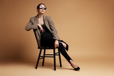 Photo of Beautiful woman in stylish outfit sitting on chair against beige background, space for text