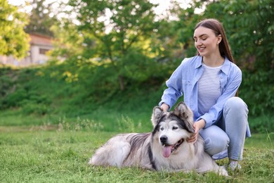 Photo of Happy woman with her cute Alaskan malamute dog on green grass outdoors. Space for text