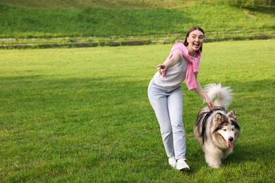 Photo of Happy woman showing something to her cute Alaskan malamute dog on green grass outdoors. Space for text