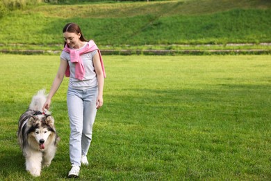 Photo of Smiling woman walking with her cute Alaskan malamute dog on green grass outdoors. Space for text