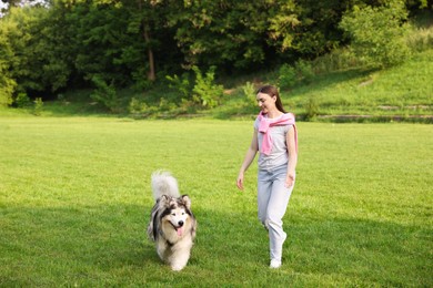 Photo of Smiling woman walking with her cute Alaskan malamute dog on green grass outdoors