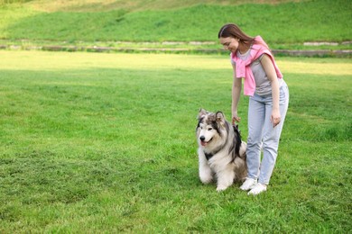 Photo of Smiling woman with her cute Alaskan malamute dog on green grass outdoors. Space for text