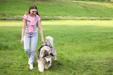 Photo of Smiling woman with her cute Alaskan malamute dog on green grass outdoors. Space for text