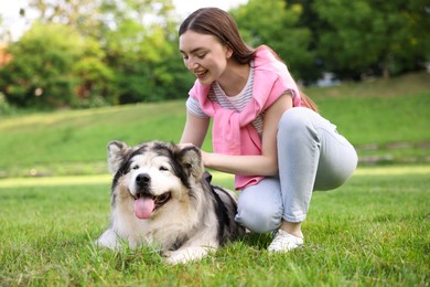 Photo of Smiling woman with her cute Alaskan malamute dog on green grass outdoors