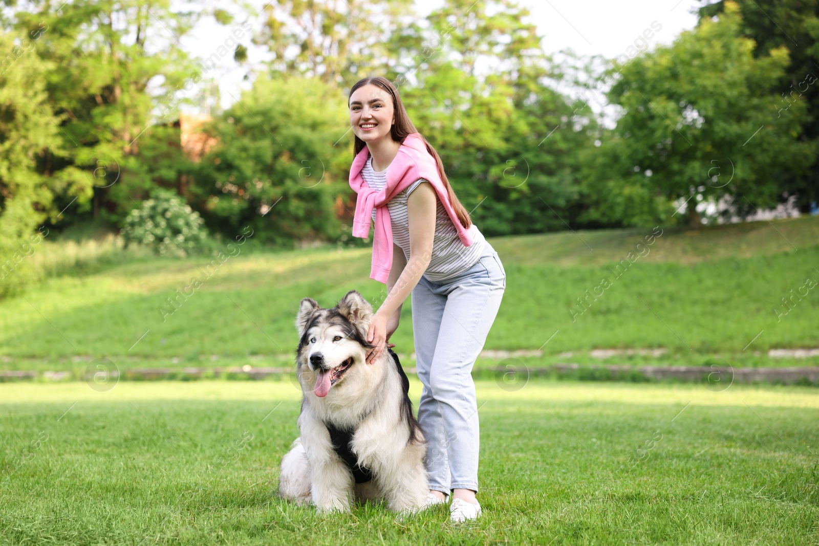 Photo of Smiling woman with her cute Alaskan malamute dog on green grass outdoors