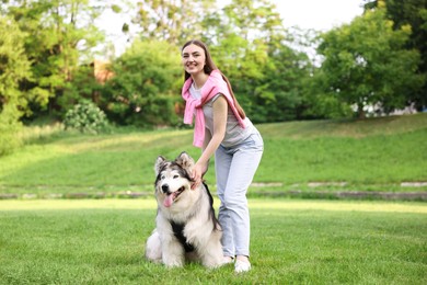 Photo of Smiling woman with her cute Alaskan malamute dog on green grass outdoors