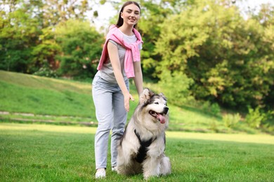 Photo of Smiling woman with her cute Alaskan malamute dog on green grass outdoors