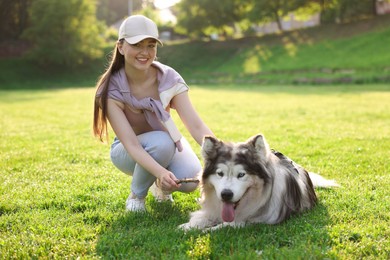 Photo of Smiling woman giving stick to her cute Alaskan malamute dog on green grass outdoors in morning