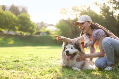 Photo of Happy woman showing something to her cute Alaskan malamute dog on green grass outdoors in morning. Space for text