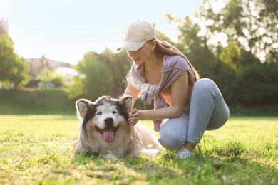 Photo of Smiling woman with her cute Alaskan malamute dog on green grass outdoors in morning