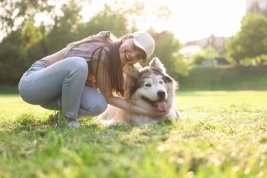 Photo of Smiling woman with her cute Alaskan malamute dog on green grass outdoors in morning
