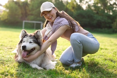 Photo of Smiling woman with her cute Alaskan malamute dog on green grass outdoors in morning