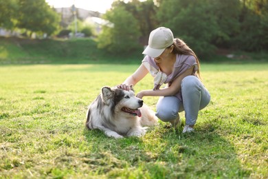 Photo of Smiling woman stroking her cute Alaskan malamute dog on green grass outdoors in morning