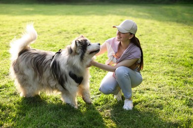Photo of Smiling woman with her cute Alaskan malamute dog on green grass outdoors in morning