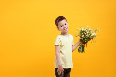Photo of Smiling little boy with bouquet of beautiful chamomile flowers on yellow background