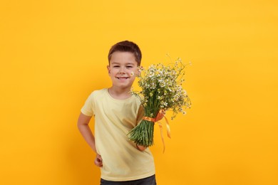 Photo of Smiling little boy with bouquet of beautiful chamomile flowers on yellow background