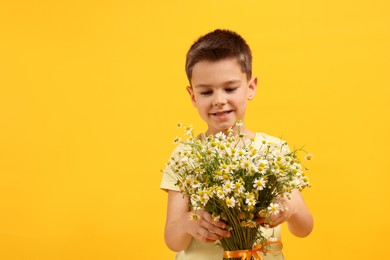 Photo of Smiling little boy with bouquet of beautiful chamomile flowers on yellow background. Space for text