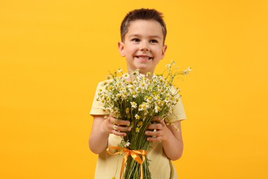 Photo of Smiling little boy with bouquet of beautiful chamomile flowers on yellow background