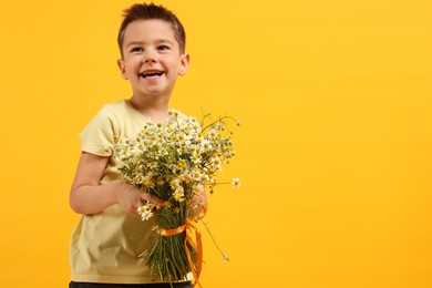 Photo of Smiling little boy with bouquet of beautiful chamomile flowers on yellow background. Space for text