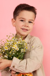 Photo of Portrait of smiling little boy with bouquet of beautiful chamomile flowers on pink background