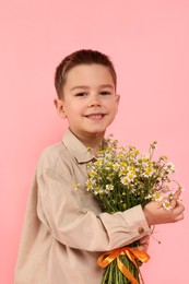Photo of Portrait of smiling little boy with bouquet of beautiful chamomile flowers on pink background