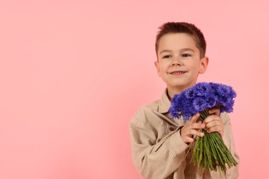 Photo of Smiling little boy with bouquet of beautiful cornflowers on pink background. Space for text