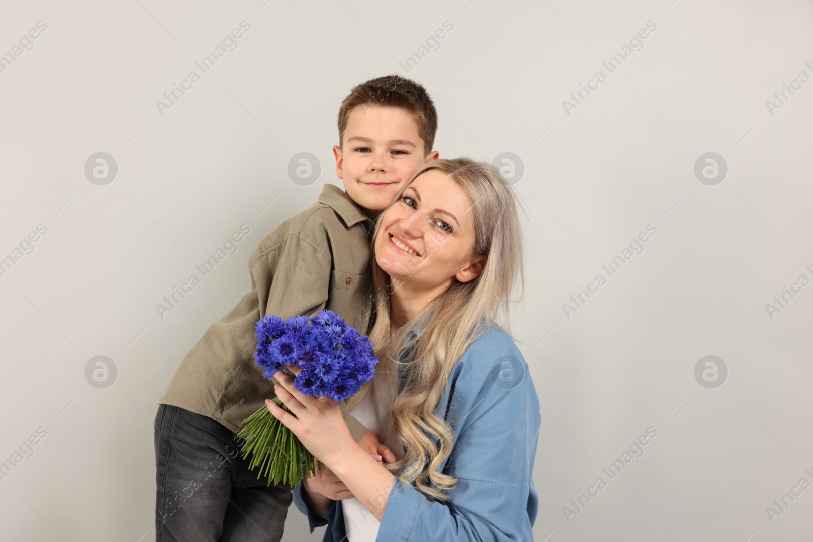Photo of Little boy and his smiling mother with bouquet of beautiful cornflowers on grey background