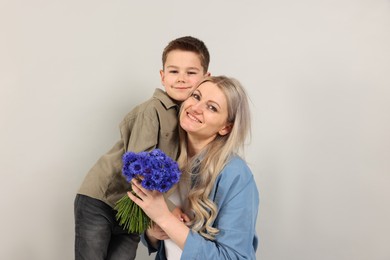 Photo of Little boy and his smiling mother with bouquet of beautiful cornflowers on grey background