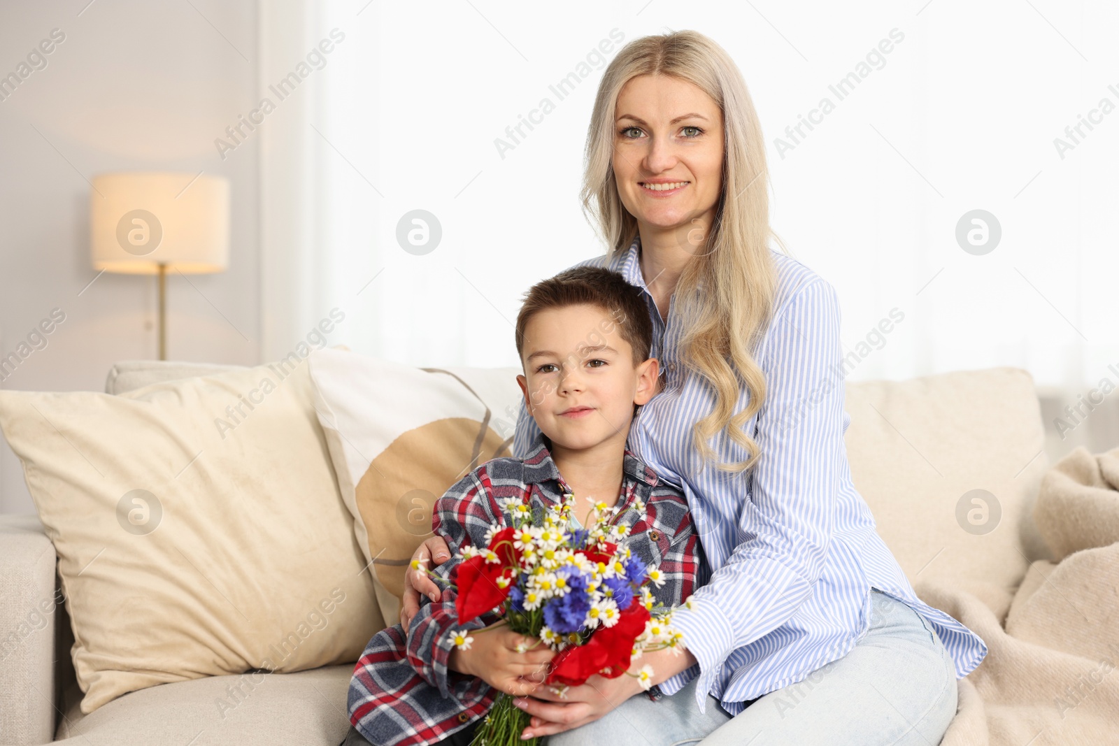 Photo of Little boy and his smiling mother with bouquet of beautiful flowers on sofa at home