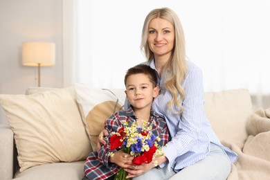 Photo of Little boy and his smiling mother with bouquet of beautiful flowers on sofa at home