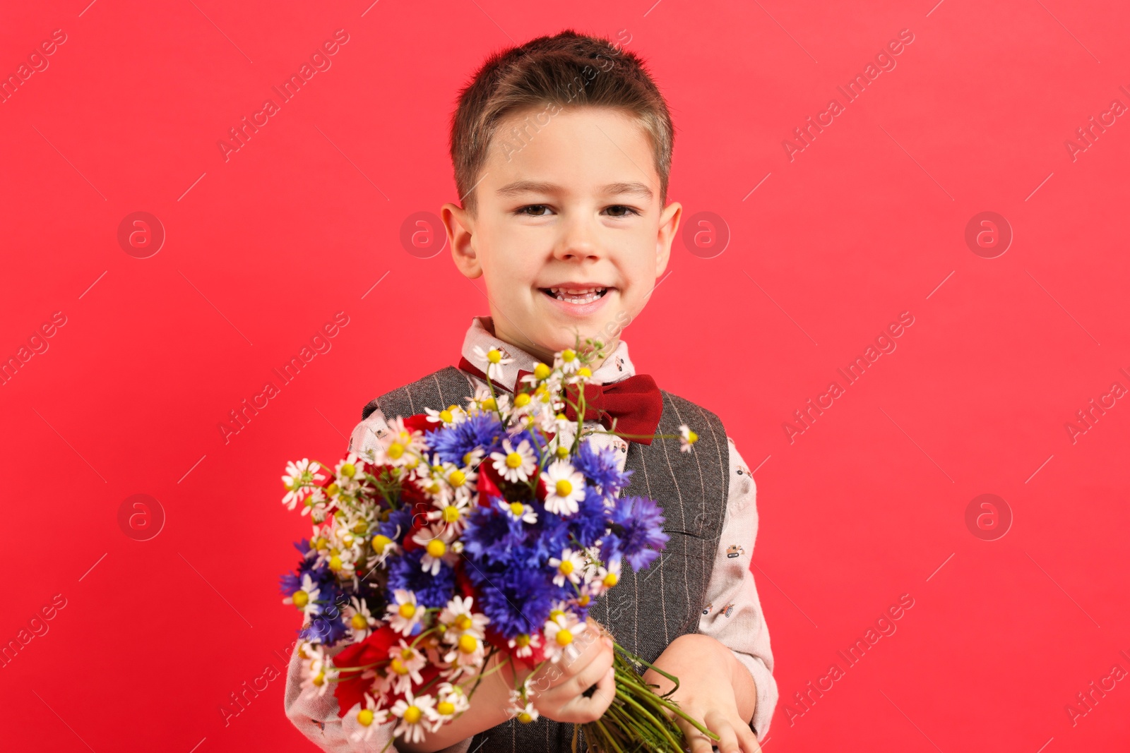 Photo of Portrait of smiling little boy with bouquet of beautiful flowers on red background