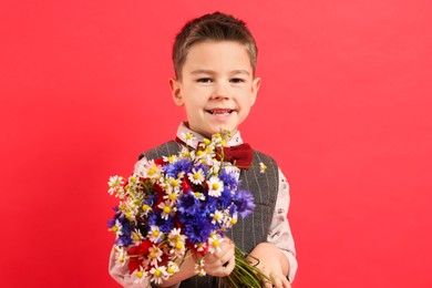 Photo of Portrait of smiling little boy with bouquet of beautiful flowers on red background