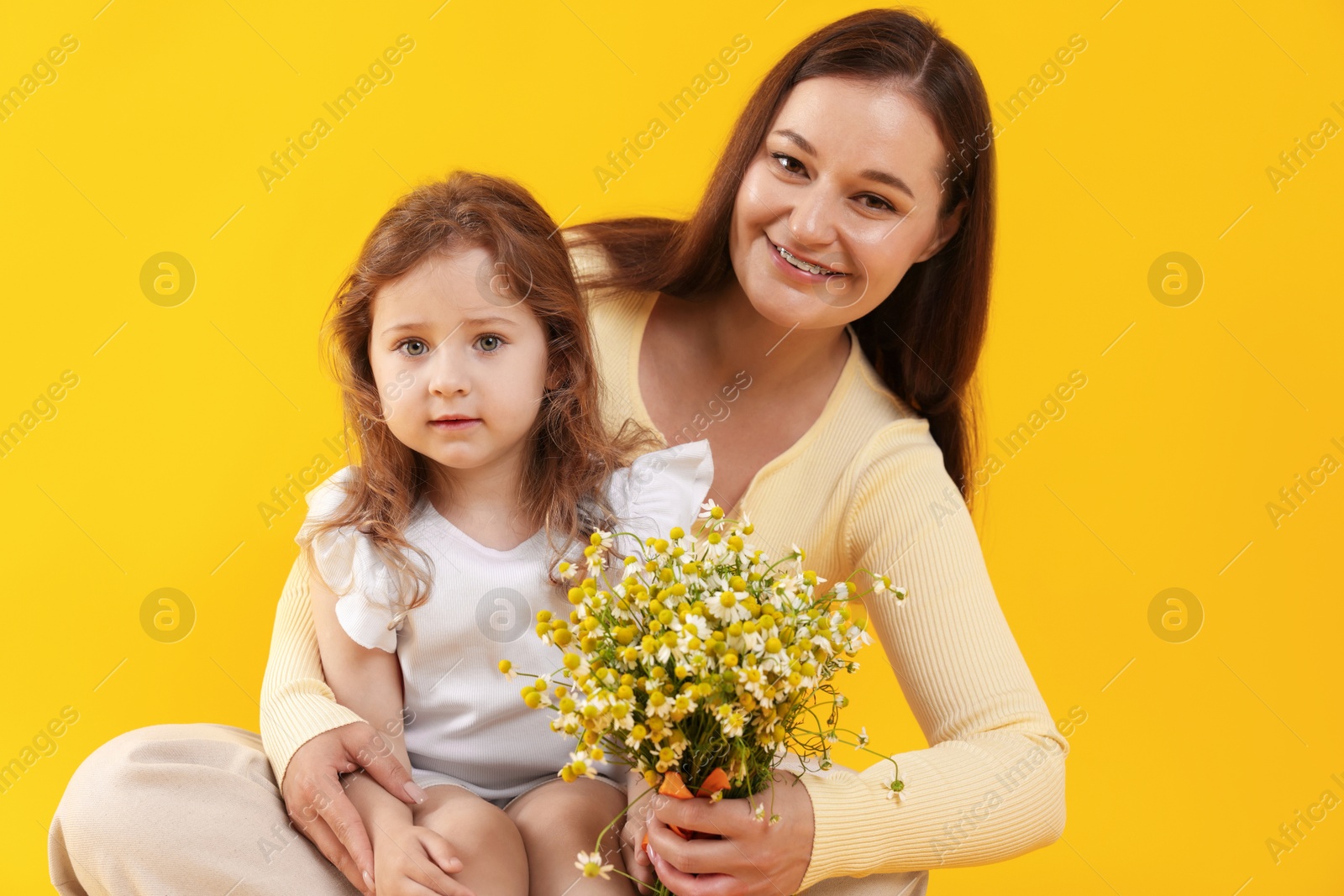 Photo of Mother and her little daughter with bouquet of beautiful chamomile flowers on orange background
