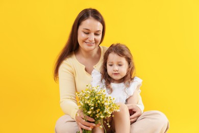 Photo of Mother and her little daughter with bouquet of beautiful chamomile flowers on orange background