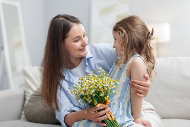 Photo of Mother and her little daughter with bouquet of beautiful chamomile flowers on sofa indoors