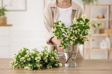 Photo of Woman making bouquet of jasmine branches at wooden table, closeup