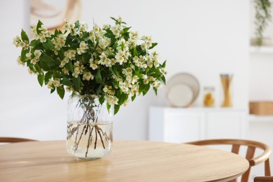 Photo of Bouquet of beautiful jasmine flowers in vase on wooden table indoors. Space for text