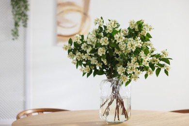 Photo of Bouquet of beautiful jasmine flowers in vase on wooden table indoors. Space for text