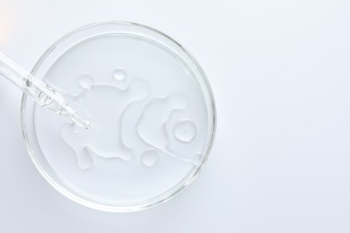 Photo of Cosmetic product and dropper in Petri dish on white background, top view