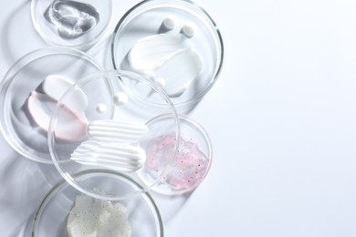 Photo of Different cosmetic products in Petri dishes on white background, flat lay. Space for text
