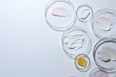 Photo of Different cosmetic products in Petri dishes on white background, flat lay. Space for text