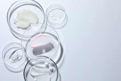 Photo of Different cosmetic products in Petri dishes on white background, flat lay. Space for text