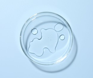 Photo of Cosmetic product in Petri dish on light blue background, top view