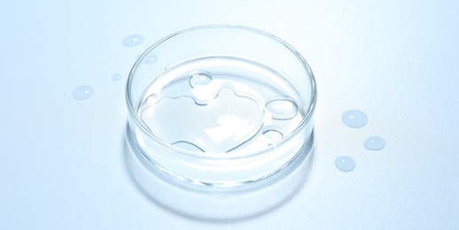 Photo of Cosmetic product in Petri dish on light blue background, closeup