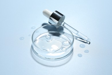 Photo of Cosmetic product in Petri dish and dropper on light blue background, closeup