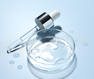 Photo of Cosmetic product in Petri dish and dropper on light blue background, closeup