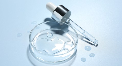Photo of Cosmetic product in Petri dish and dropper on light blue background, closeup