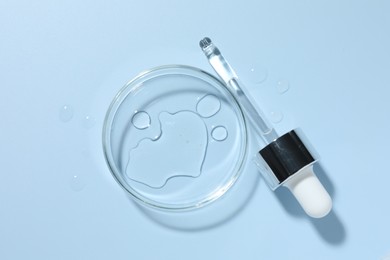 Photo of Cosmetic product in Petri dish and dropper on light blue background, top view